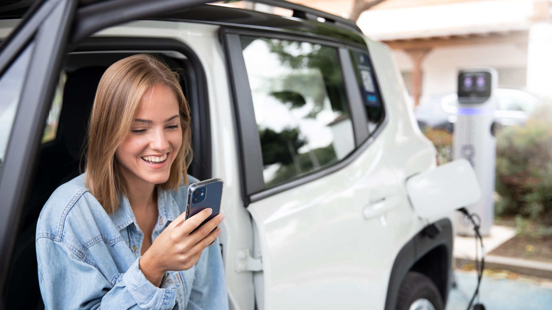 Frau mit Smartphone im E-Auto an einer Ladesäule